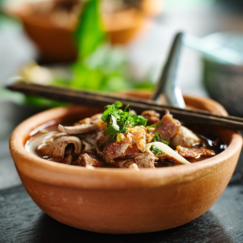 thai bowl of beef noodle soup in clay pot with duck liver